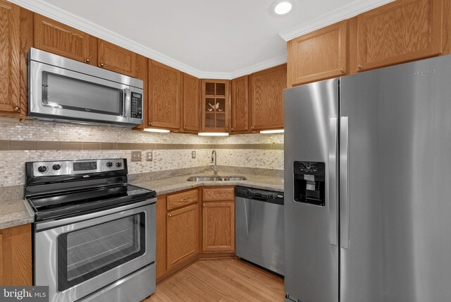 kitchen with light stone counters, light hardwood / wood-style flooring, sink, ornamental molding, and appliances with stainless steel finishes