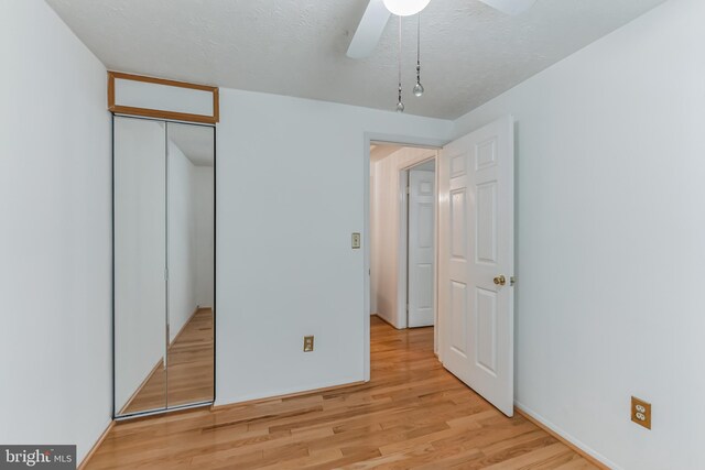 unfurnished bedroom featuring ceiling fan, a textured ceiling, a closet, and light wood-type flooring