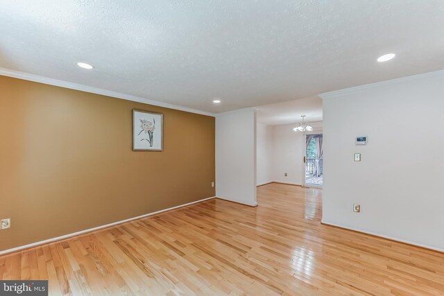 empty room with an inviting chandelier, light hardwood / wood-style flooring, and crown molding