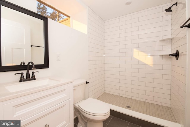 bathroom featuring toilet, a tile shower, vanity, and tile patterned floors