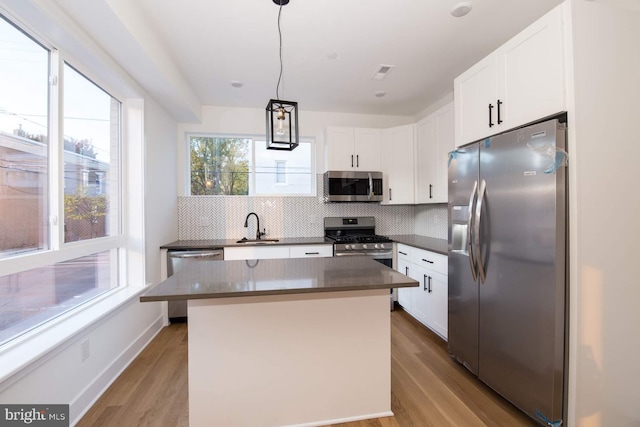 kitchen with a kitchen island, pendant lighting, appliances with stainless steel finishes, and light hardwood / wood-style flooring