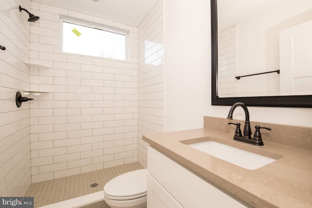 bathroom with a tile shower, vanity, and toilet