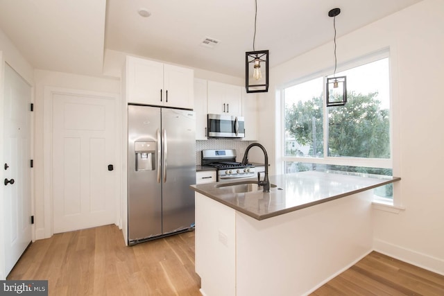 kitchen featuring white cabinetry, appliances with stainless steel finishes, backsplash, hanging light fixtures, and light hardwood / wood-style floors