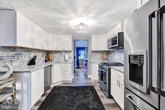 kitchen with white cabinets, hardwood / wood-style flooring, decorative backsplash, appliances with stainless steel finishes, and light stone counters