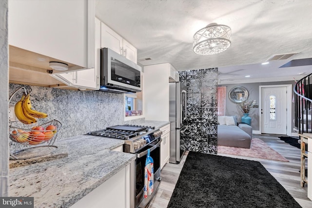 kitchen with appliances with stainless steel finishes, light wood-type flooring, light stone counters, a notable chandelier, and white cabinets