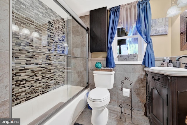 full bathroom with tile patterned floors, bath / shower combo with glass door, vanity, tile walls, and toilet