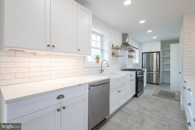 kitchen with light stone countertops, backsplash, stainless steel appliances, wall chimney range hood, and white cabinets