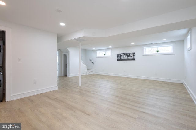 basement featuring stacked washer / dryer, light hardwood / wood-style flooring, and a healthy amount of sunlight