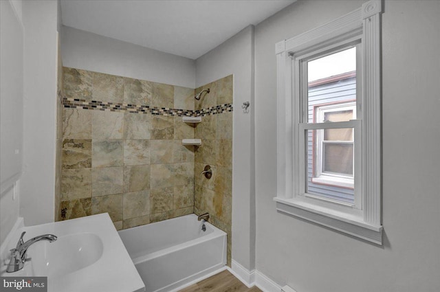 bathroom with hardwood / wood-style floors, tiled shower / bath combo, and sink