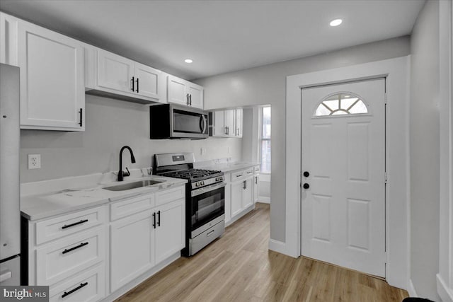 kitchen with light stone countertops, sink, stainless steel appliances, light hardwood / wood-style floors, and white cabinets