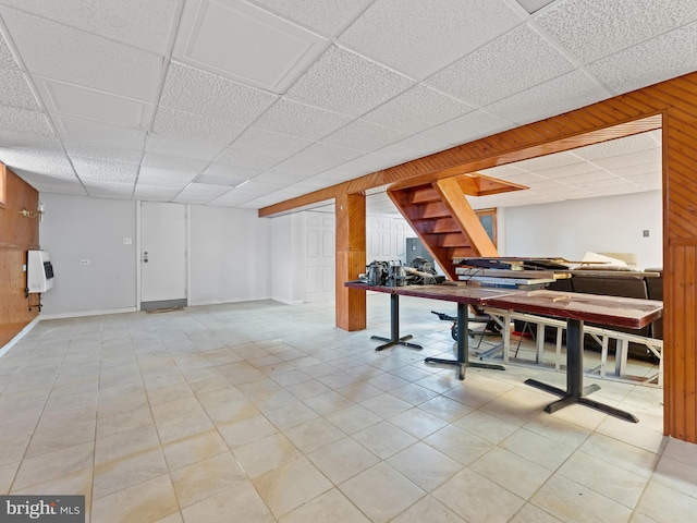 basement featuring wood walls, a paneled ceiling, light tile patterned floors, and heating unit