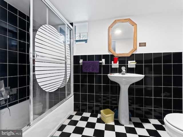 bathroom featuring tile walls, enclosed tub / shower combo, and toilet