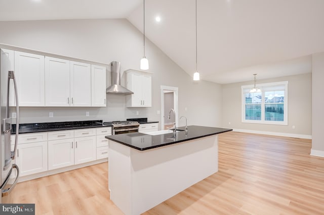 kitchen featuring stainless steel appliances, wall chimney range hood, pendant lighting, a center island with sink, and white cabinets