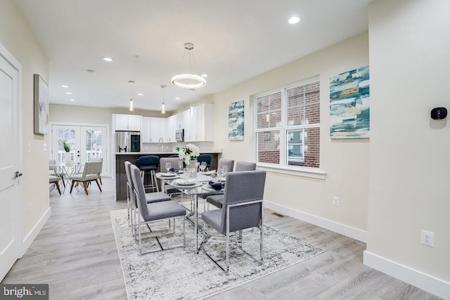 dining space with sink, light wood-type flooring, and french doors