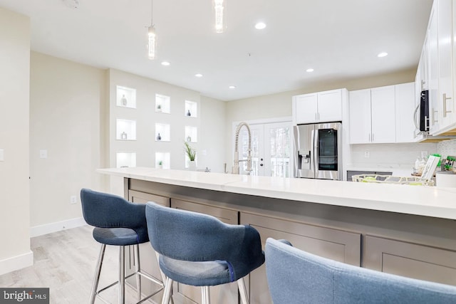 kitchen featuring stainless steel appliances, light hardwood / wood-style floors, white cabinetry, tasteful backsplash, and hanging light fixtures