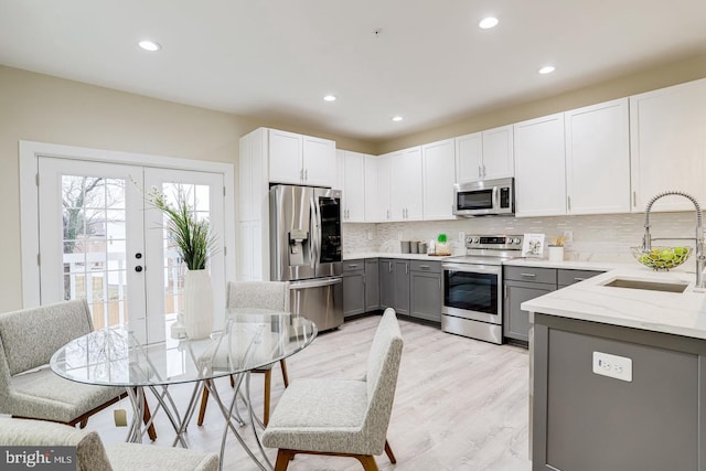 kitchen with stainless steel appliances, white cabinetry, sink, gray cabinetry, and light wood-type flooring