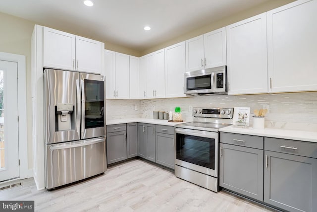 kitchen with backsplash, appliances with stainless steel finishes, gray cabinets, white cabinets, and light hardwood / wood-style flooring