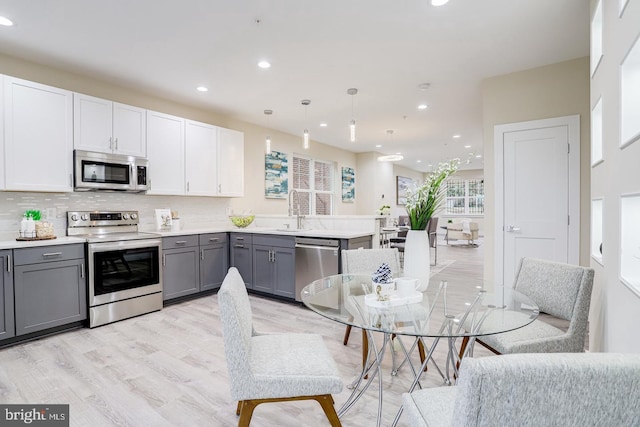 kitchen with pendant lighting, stainless steel appliances, white cabinets, and gray cabinetry