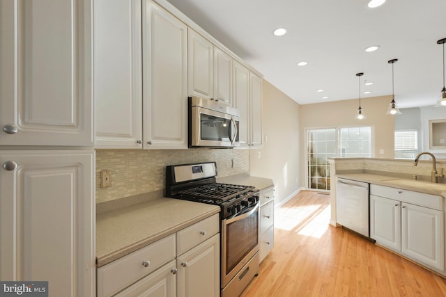 kitchen with light wood-type flooring, stainless steel appliances, sink, pendant lighting, and white cabinets