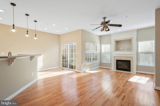 unfurnished living room featuring ceiling fan, a healthy amount of sunlight, light wood-type flooring, and sink