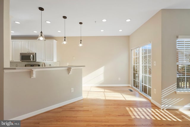 kitchen featuring a breakfast bar area, white cabinetry, pendant lighting, and light wood-type flooring