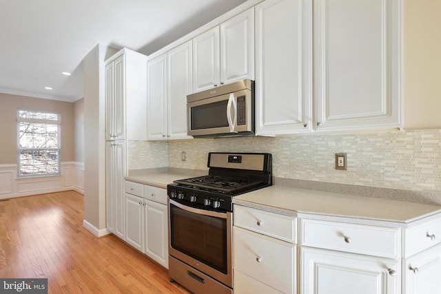 kitchen featuring white cabinets, crown molding, tasteful backsplash, light hardwood / wood-style floors, and stainless steel appliances