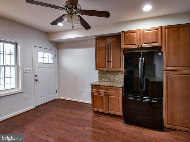 kitchen with tasteful backsplash, black fridge, light stone counters, and dark hardwood / wood-style floors