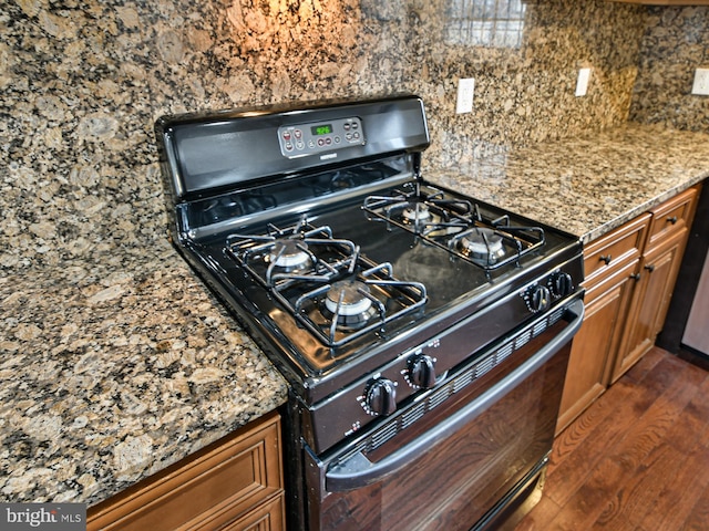 kitchen with dark hardwood / wood-style flooring, black range with gas stovetop, backsplash, and stone countertops