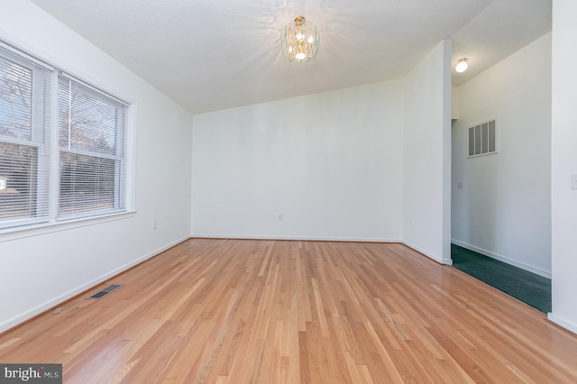 empty room with a notable chandelier, light hardwood / wood-style floors, and a textured ceiling