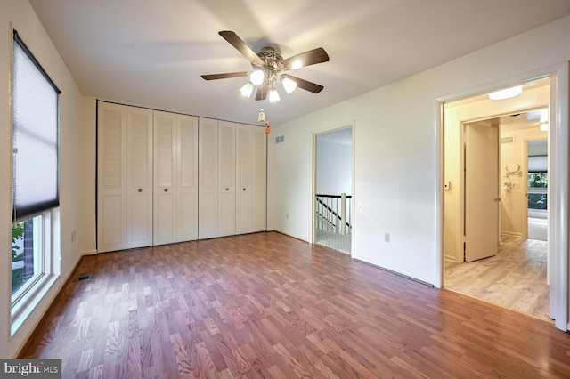 unfurnished bedroom with a closet, multiple windows, wood-type flooring, and ceiling fan