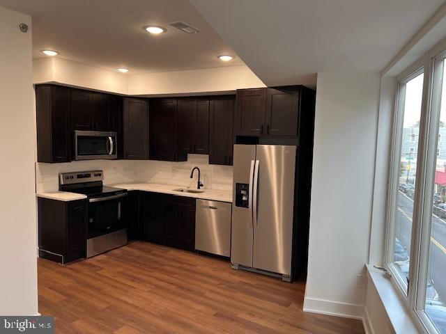 kitchen featuring dark brown cabinetry, light hardwood / wood-style flooring, sink, tasteful backsplash, and appliances with stainless steel finishes