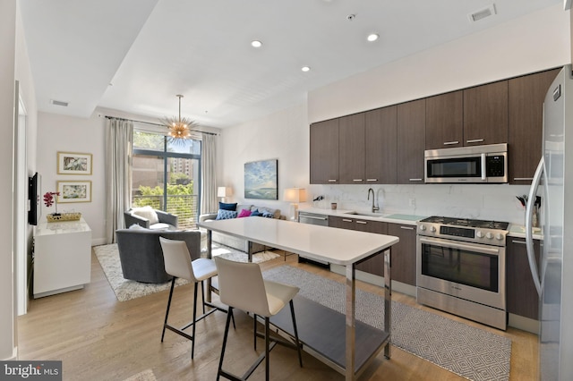 kitchen with stainless steel appliances, dark brown cabinetry, hanging light fixtures, sink, and light hardwood / wood-style flooring