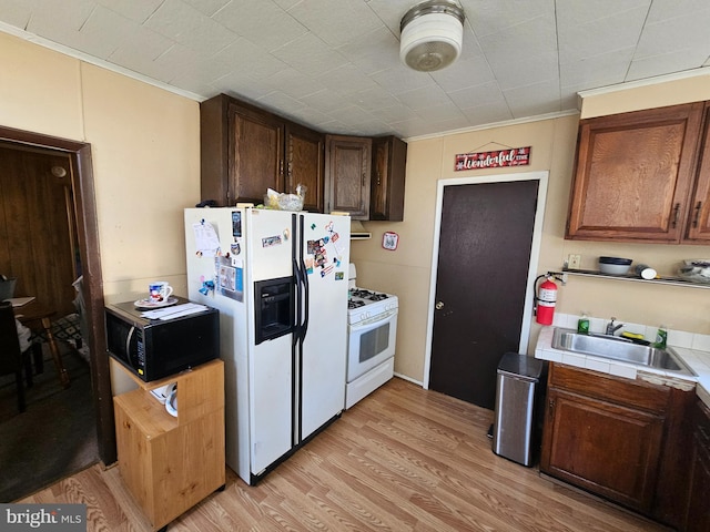 kitchen featuring ornamental molding, light wood-type flooring, sink, tile countertops, and white appliances