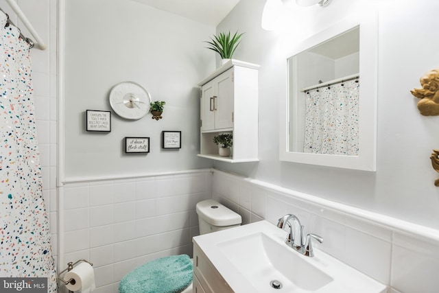 bathroom featuring walk in shower, vanity, toilet, and tile walls