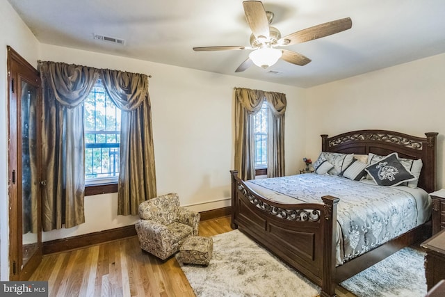 bedroom with wood-type flooring, baseboard heating, multiple windows, and ceiling fan