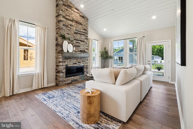 living room with a stone fireplace, high vaulted ceiling, and light hardwood / wood-style flooring