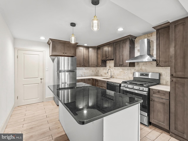 kitchen with wall chimney exhaust hood, light hardwood / wood-style flooring, a kitchen island, pendant lighting, and appliances with stainless steel finishes