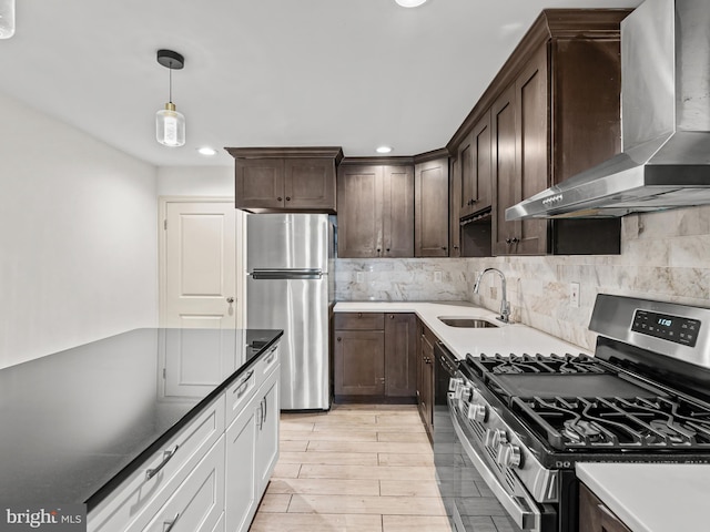 kitchen featuring white cabinetry, wall chimney range hood, appliances with stainless steel finishes, hanging light fixtures, and sink