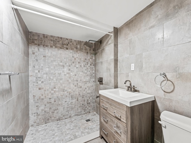 bathroom with tile walls, tiled shower, vanity, and toilet