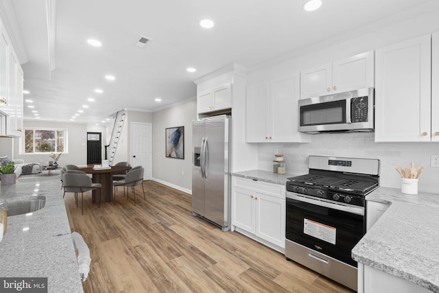 kitchen with stainless steel appliances, light hardwood / wood-style floors, light stone counters, white cabinets, and ornamental molding