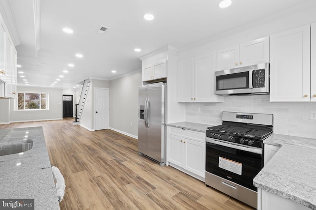 kitchen featuring light hardwood / wood-style floors, light stone counters, appliances with stainless steel finishes, white cabinets, and decorative backsplash