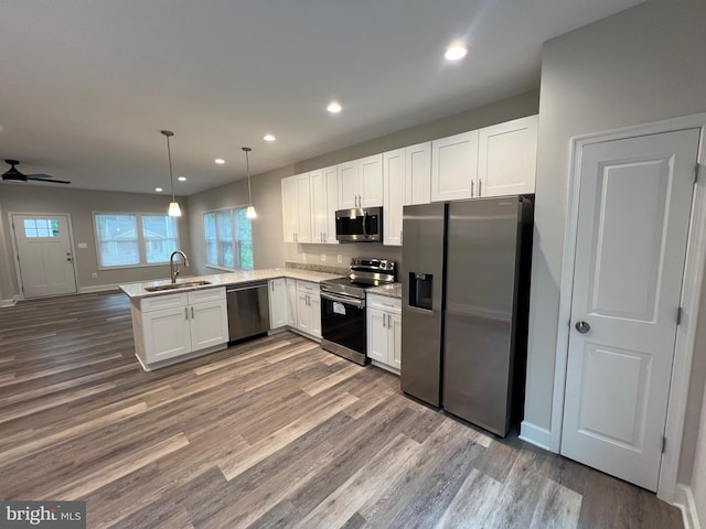 kitchen with sink, kitchen peninsula, hanging light fixtures, white cabinetry, and stainless steel appliances