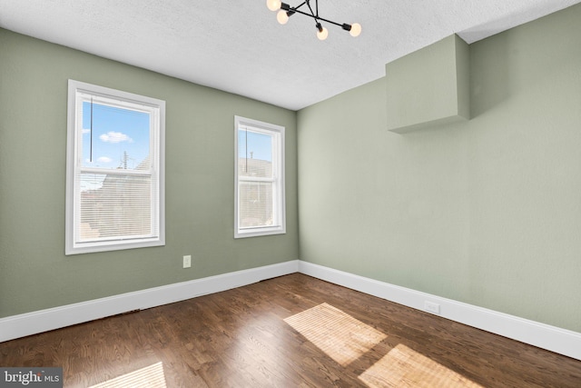 spare room featuring a wealth of natural light, a textured ceiling, an inviting chandelier, and dark hardwood / wood-style flooring