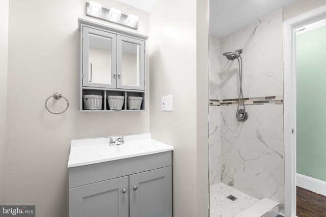 bathroom with tiled shower, vanity, and wood-type flooring