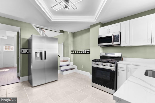 kitchen with white cabinets, a raised ceiling, light stone counters, and appliances with stainless steel finishes