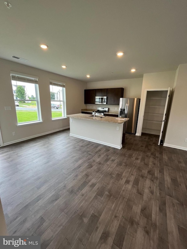 kitchen with sink, dark hardwood / wood-style flooring, a kitchen island with sink, light stone counters, and stainless steel appliances