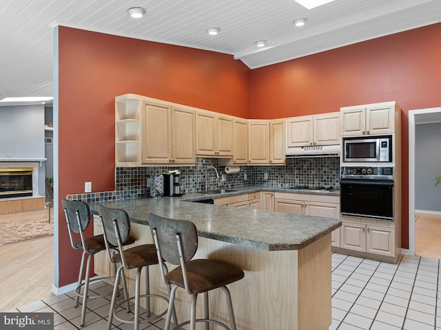 kitchen featuring sink, a breakfast bar, kitchen peninsula, black oven, and stainless steel microwave