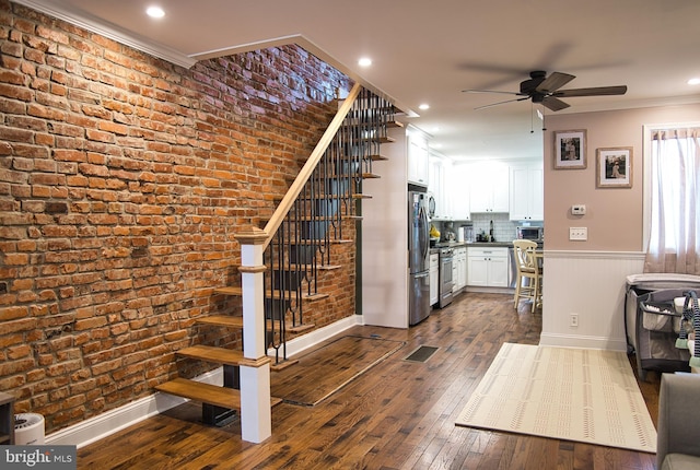 staircase with brick wall, wood-type flooring, ceiling fan, and crown molding