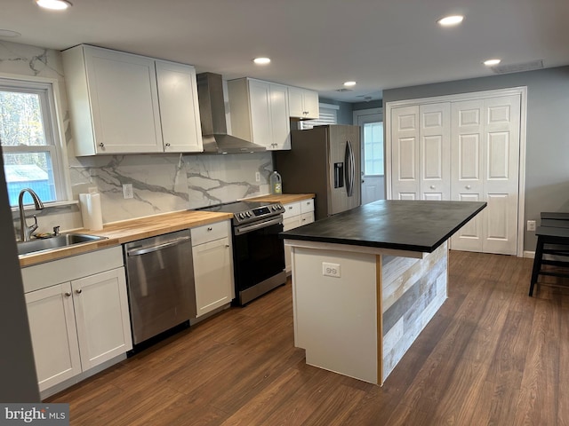 kitchen featuring dark wood-type flooring, wall chimney exhaust hood, a kitchen island, white cabinetry, and stainless steel appliances