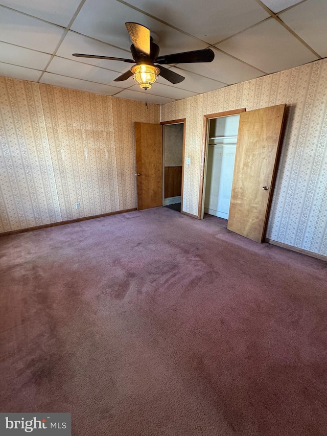 unfurnished bedroom with carpet floors, a paneled ceiling, ceiling fan, and two closets